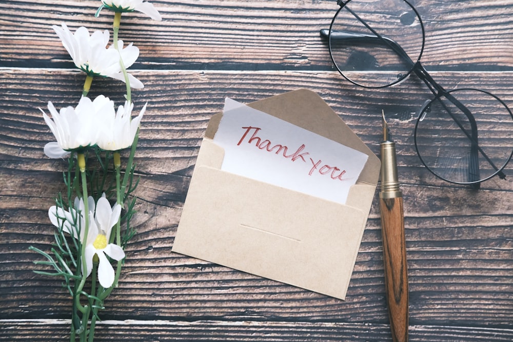 a thank you note sitting on top of a table next to a pair of glasses