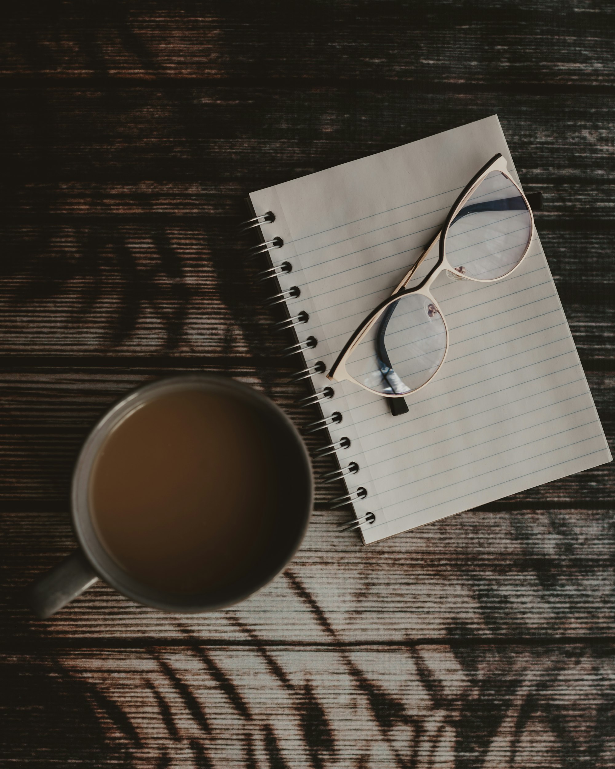 a cup of coffee next to a notepad with a pair of glasses on it