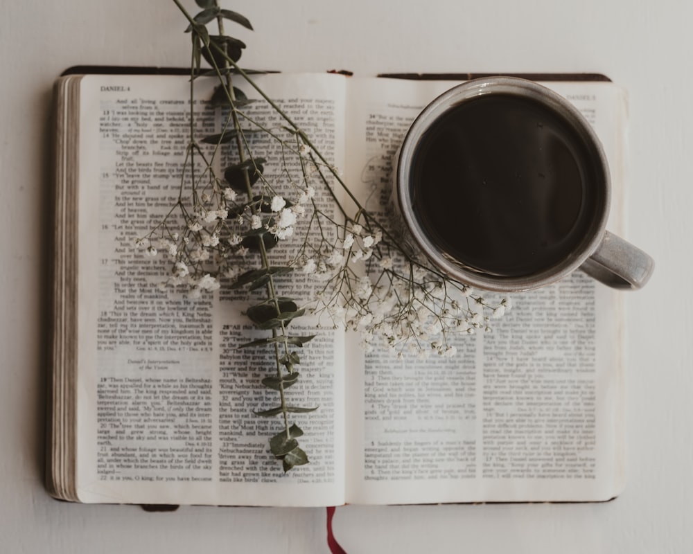 a cup of coffee and some flowers on an open book