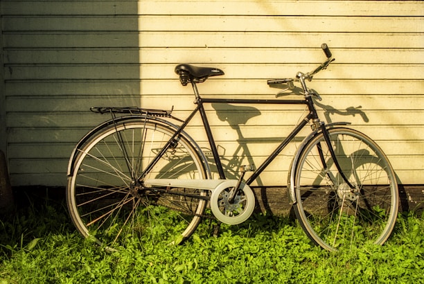 A vintage bicycle leaning against a workshop wall with warm sunlight casting shadows.