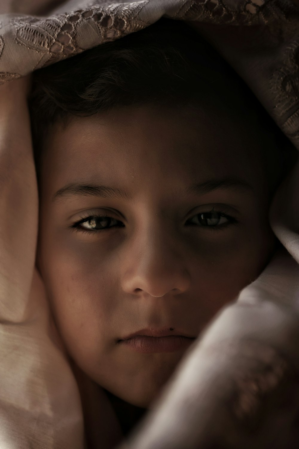a young boy is hiding under a blanket