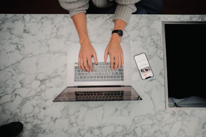 a person typing on a laptop on a marble table