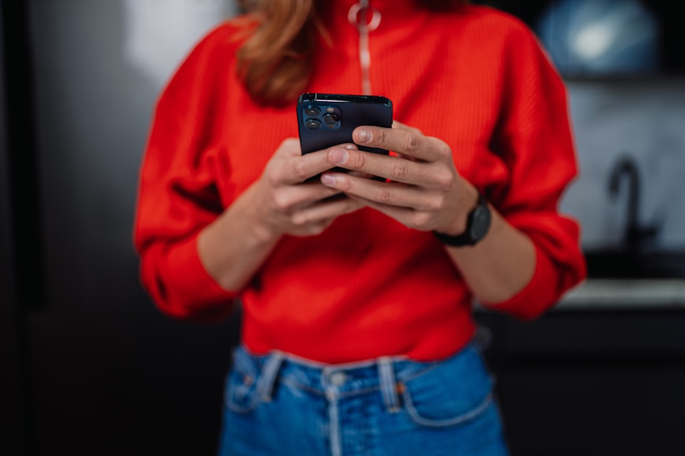 a woman in a red shirt is holding a cell phone
