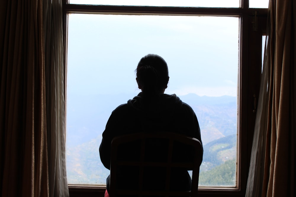 a person sitting in a chair looking out a window