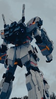 A large, humanoid robot with articulated joints and angular, armored plating stands prominently against a cloudy sky. The structure features intricate mechanical detailing and vibrant glowing lights accentuating its robust form.