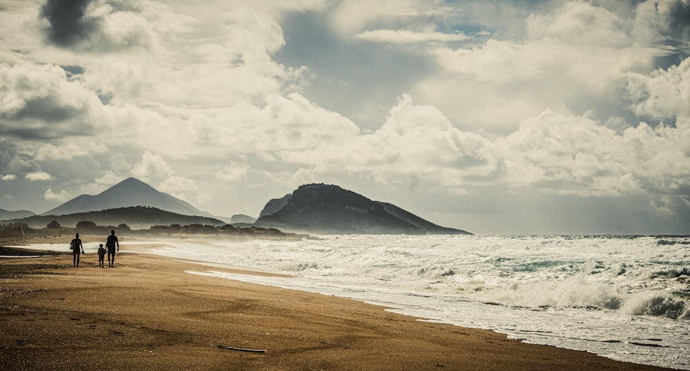 a couple of people walking along a beach next to the ocean