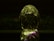 A decorative, transparent crystal object shaped like an egg with intricate carvings and patterns reflecting light. It features subtle iridescent colors on a dark background, and the object is mirrored against a surface.