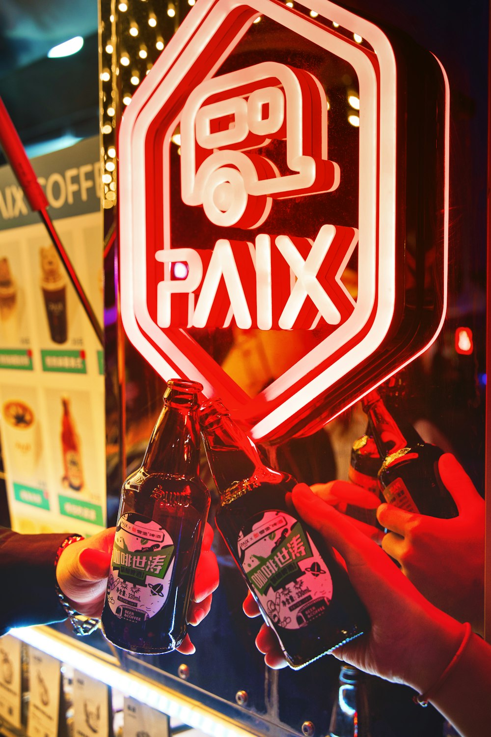 a person holding two bottles of beer in front of a neon sign