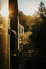 A scenic train winding through lush green mountains under a golden sunset.