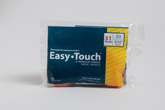A package of Easy Touch U-100 insulin syringes is displayed. It contains 10 syringes with 31 gauge, 5/16 inch length, and 0.5 mL capacity. The packaging features a combination of dark blue and yellow colors, with text emphasizing comfort and specifications.