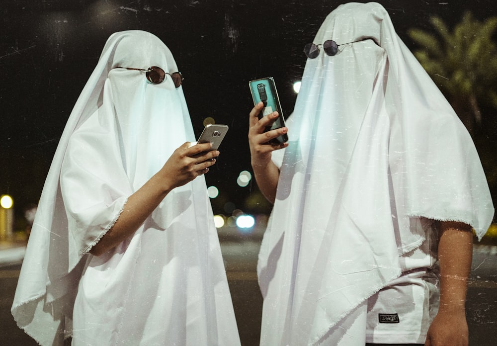 two people dressed in white are looking at a cell phone