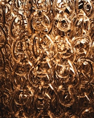 A dense cluster of translucent, intertwined acrylic chains with a golden hue, creating an intricate and luxurious texture. The light shines through them, adding a warm, glowing effect.
