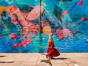 a woman in a red dress is holding a stick in front of a colorful wall