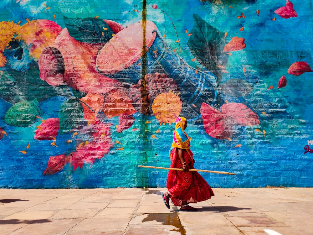 a woman in a red dress is holding a stick in front of a colorful wall