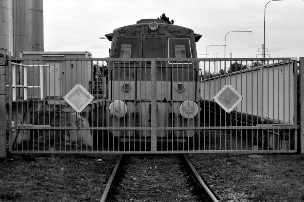 a black and white photo of a train behind a fence