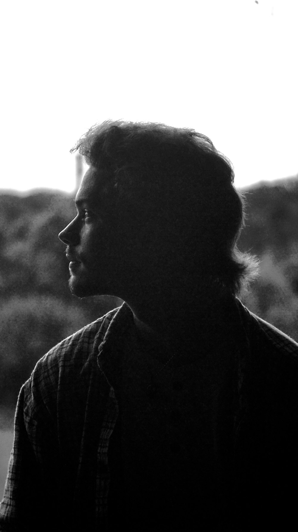 a black and white photo of a man looking out a window