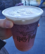 Hands holding a personalized Magic Cup with Disney charms and a pastel sleeve.