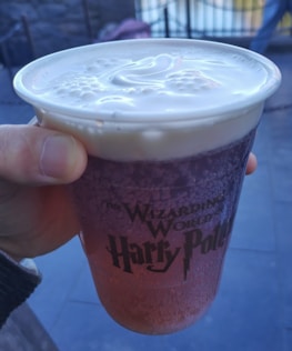 Hands holding a personalized Magic Cup with Disney charms and a pastel sleeve.