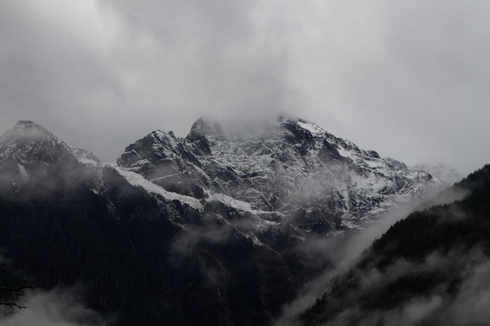 a mountain covered in snow and clouds under a cloudy sky