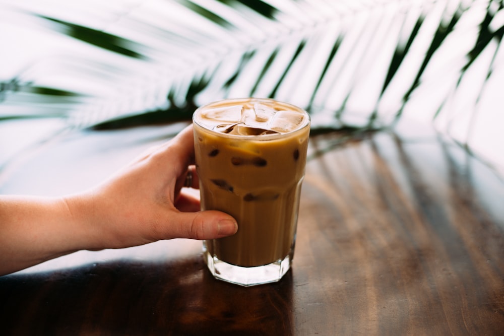 a hand holding a glass of iced coffee