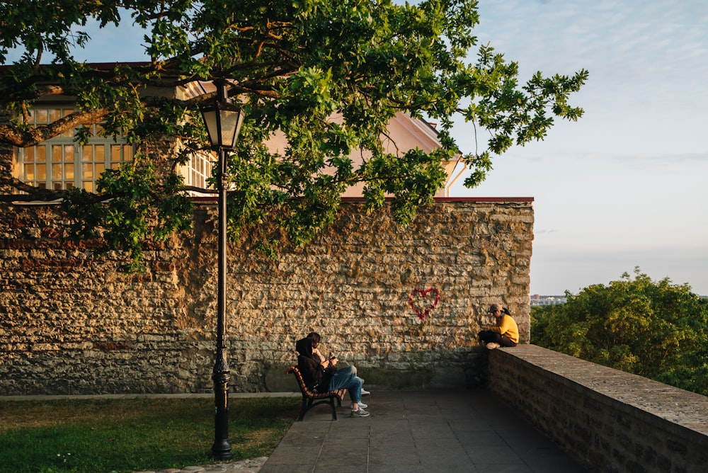two people sitting on a bench next to a stone wall