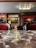 An elegant, classic interior with plush red velvet chairs and intricate black detailing. A reflective marble table is in the foreground. The room features wooden paneling, column details, and a decorative ceiling light. Portraits and antiques adorn the warm-toned walls.