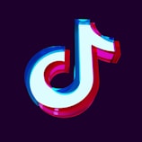 A three-dimensional logo featuring a stylized musical note symbol with vibrant neon colors, including blue, red, and white. The symbol has a glossy finish and stands out against a dark purple background.