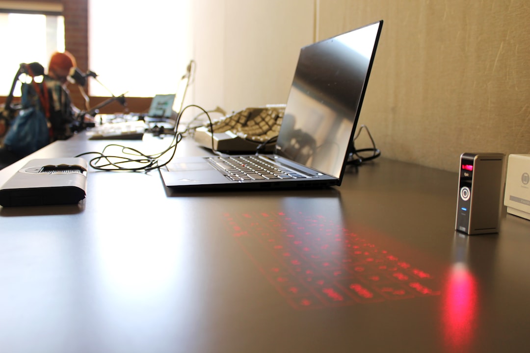 a laptop computer sitting on top of a wooden desk, A virtual keyboard displayed next to a laptop. A person in a wheelcha