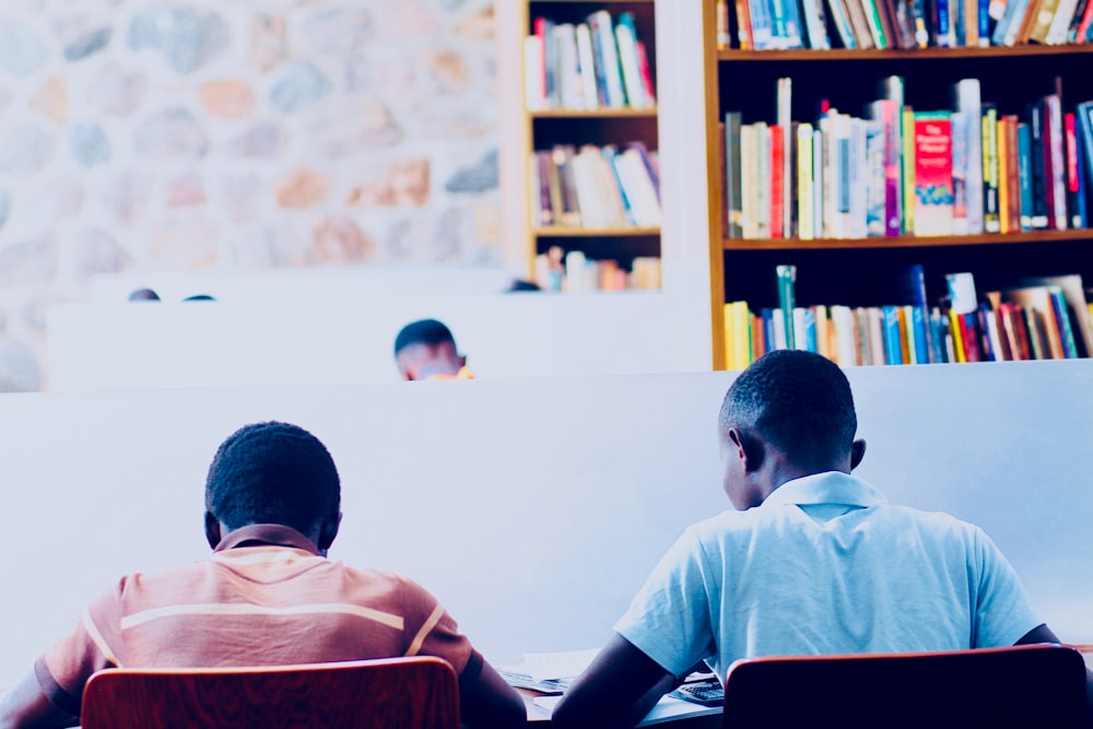 a couple of men sitting at a table in front of a book shelf