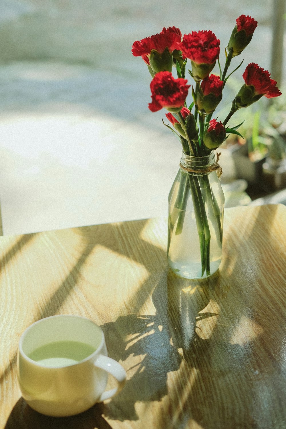 a vase of red carnations sitting on a table next to a cup of