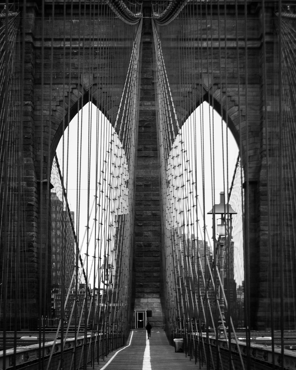 a black and white photo of a man walking across a bridge