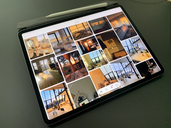 A tablet displaying a collection of interior design photos, showcasing rooms bathed in warm sunlight. The images feature modern, stylish living spaces with large windows, cozy seating, and decorative elements.