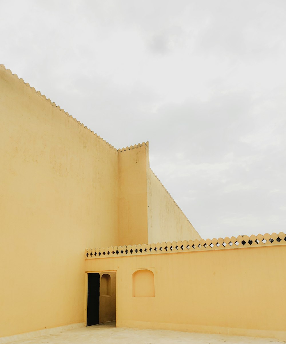 a yellow building with a black door and a sky background