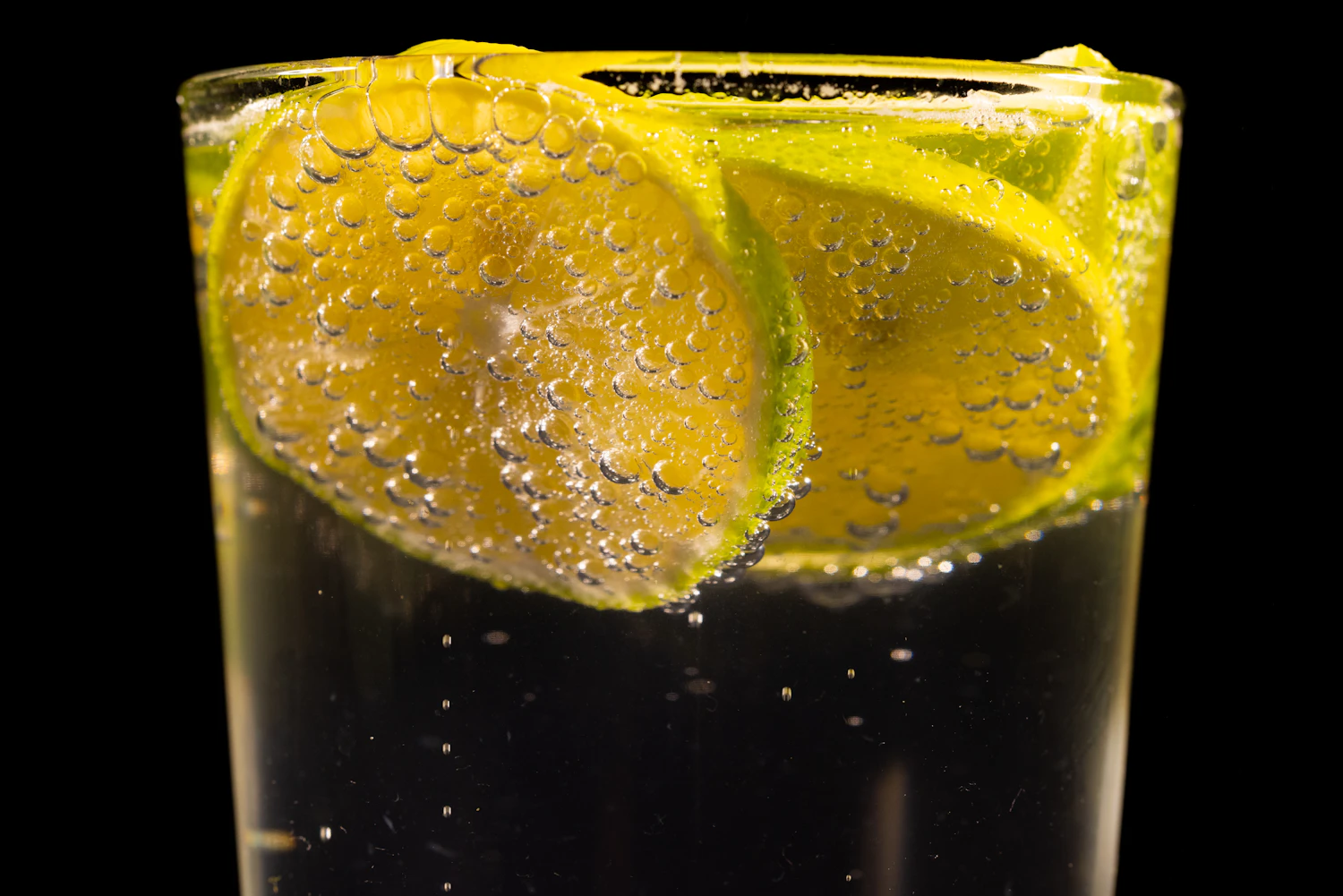 Lime wheels pressed against the side of a glass of fizzing soda, bubbles rising on black
