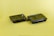 Two black plastic food containers with transparent lids are positioned on a solid yellow surface. The containers have separate compartments inside, designed for holding different types of food.
