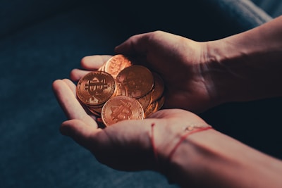 Hands holding multiple physical coins with the Bitcoin logo, suggesting a representation of cryptocurrency or digital currency in a tangible form.