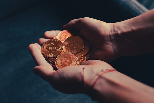 Hands holding multiple physical coins with the Bitcoin logo, suggesting a representation of cryptocurrency or digital currency in a tangible form.
