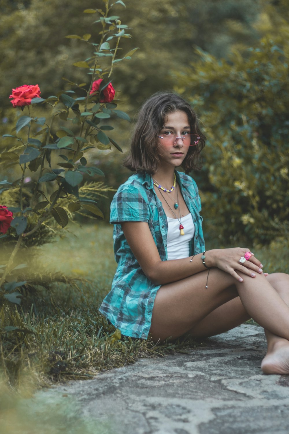 a woman sitting on a rock in front of a rose bush