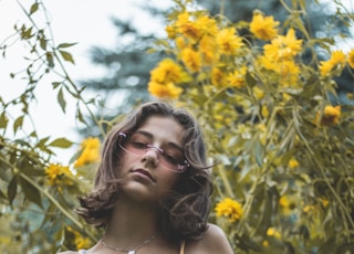 A beautiful young girl posing in front of some pretty yellow flowers.