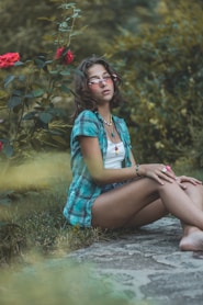 a woman sitting on the ground in front of a rose bush