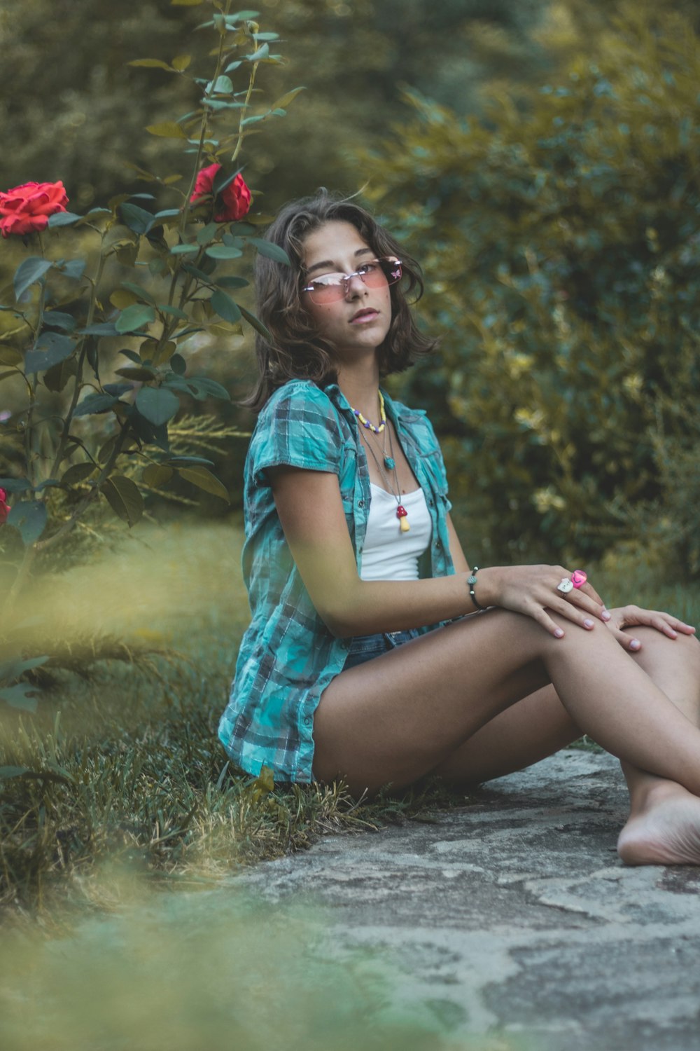 a woman sitting on the ground in front of a rose bush