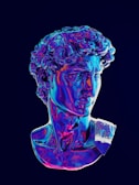 A digital artwork featuring a classical sculpture bust, vividly rendered in iridescent colors. The surface of the sculpture exhibits a blend of neon blues, purples, and pinks, giving it a surreal and modern look against a dark background.