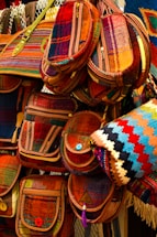 A collection of colorful, woven bags with intricate patterns, featuring various shades of red, orange, and blue. The bags have button closures and are arranged in a layered display, giving a vibrant and artistic impression.