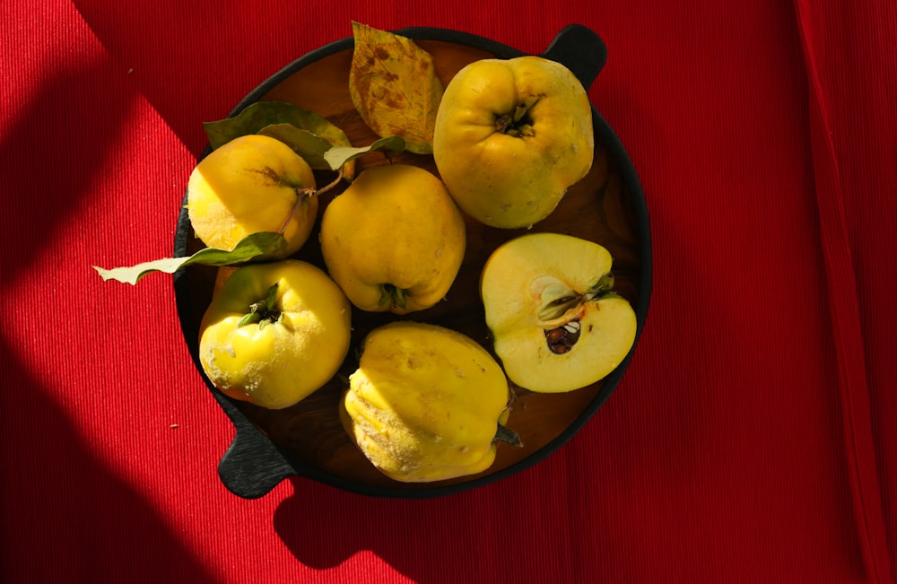 a bowl filled with yellow apples on top of a red table