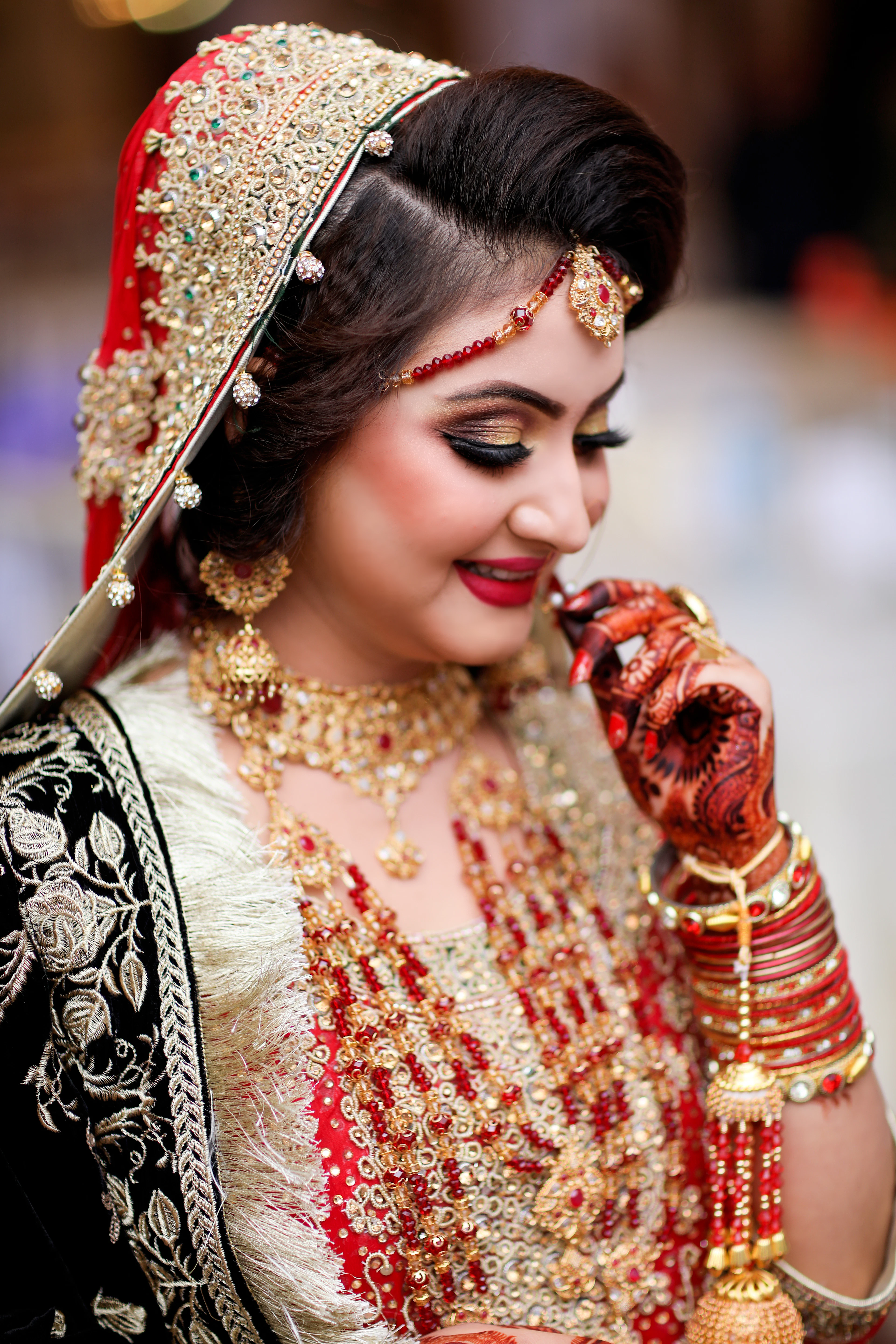 A bride with henna-painted hands wearing a maang tikka and layered gold necklaces