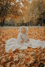 a baby doll sitting on a blanket in the leaves