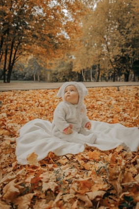 a baby doll sitting on a blanket in the leaves