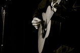 Close-up of hands playing an acoustic guitar in a dimly lit room.