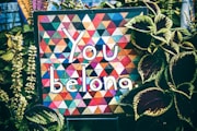 a sign that says you belong surrounded by plants