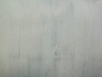 A textured surface with a rough, stucco-like finish in a muted grey-green color. The texture includes subtle vertical streaks and variations in shading.